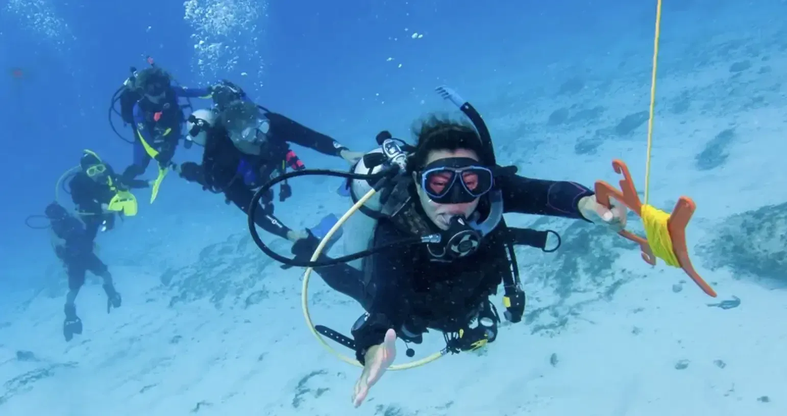 Two scuba divers underwater, one in foreground with mask and orange fins, holding a guide line