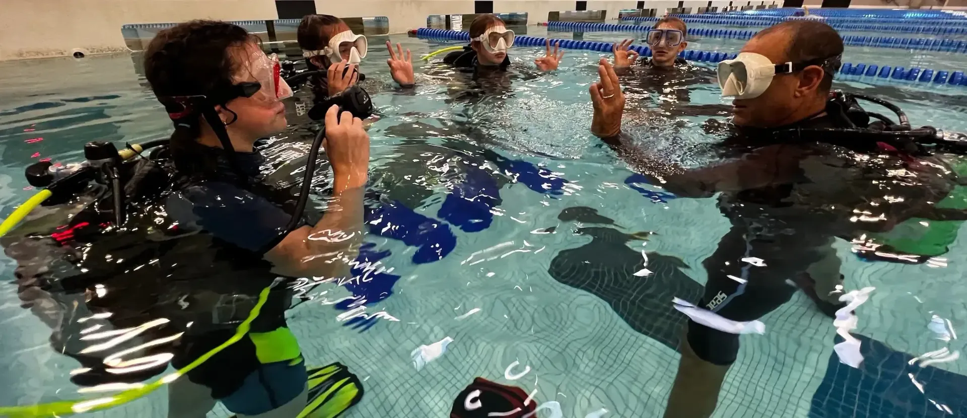 People in swim gear practicing underwater breathing in a pool with a trainer