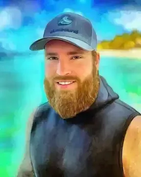 Smiling man in a blue cap and black sleeveless shirt standing by a tropical beach