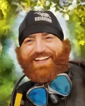 Smiling bearded person in a black beanie and blue snorkel mask against a leafy background