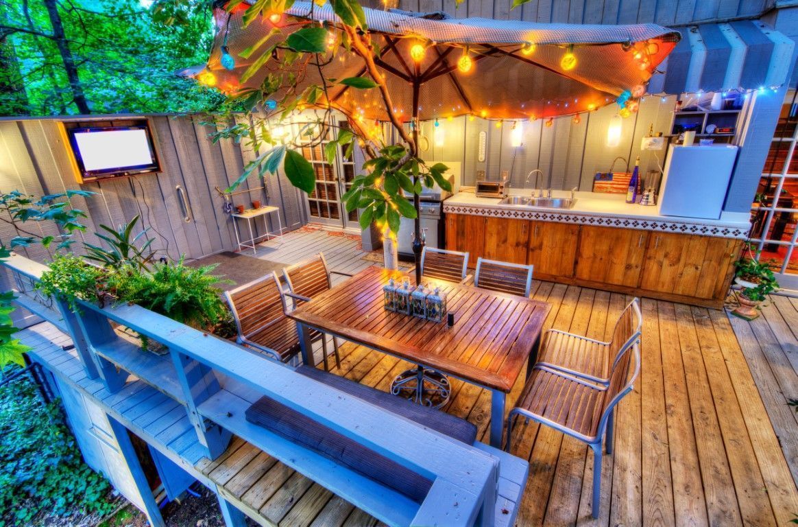 Wooden rooftop deck with string lights, picnic table, benches, and a small bar at dusk