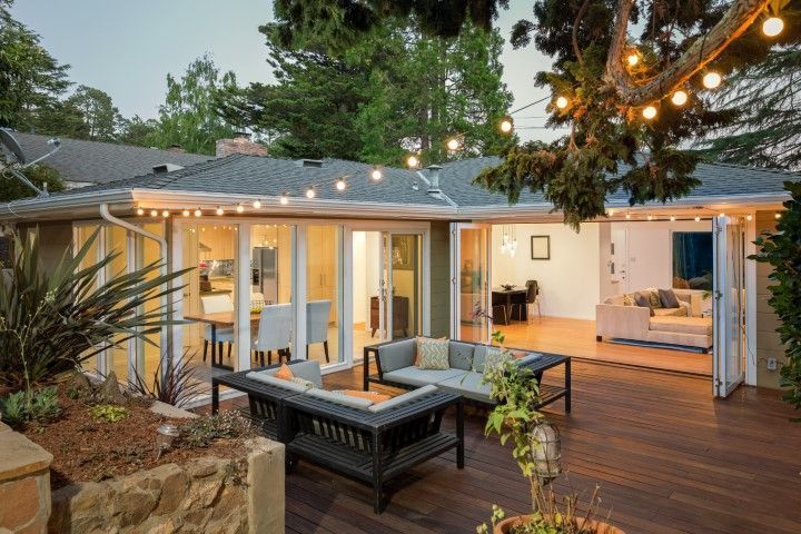 Cozy backyard patio with string lights, cushioned seating, fire pit, and open house doors at dusk