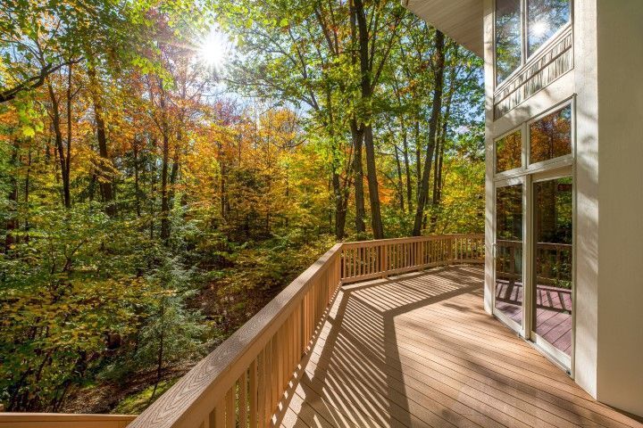 Wooden deck beside a glass house overlooking sunlit autumn forest trees
