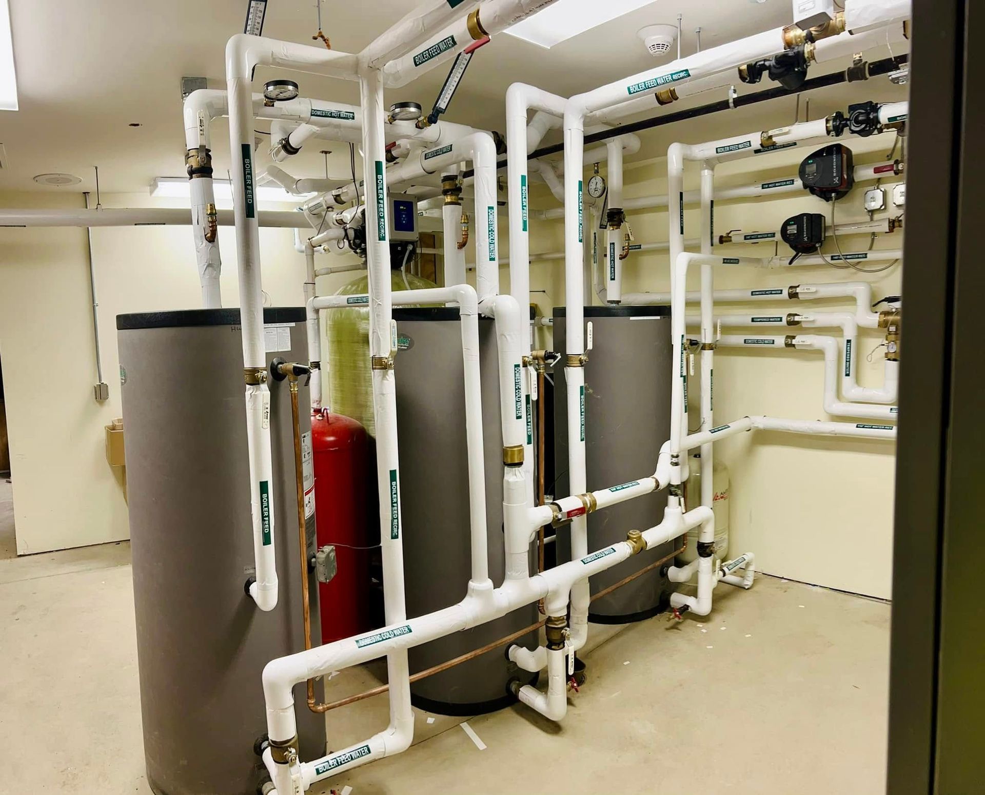 Industrial basement with gray tanks, white pipes, and red equipment in a mechanical room