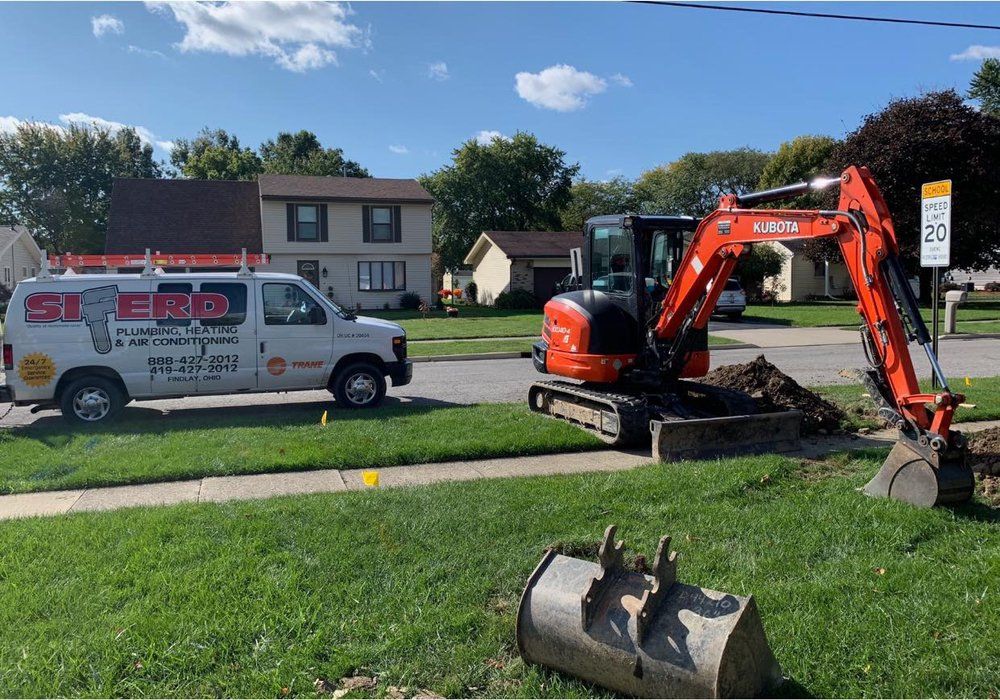 Orange excavator digging a trench on a suburban lawn beside a service van on a sunny day