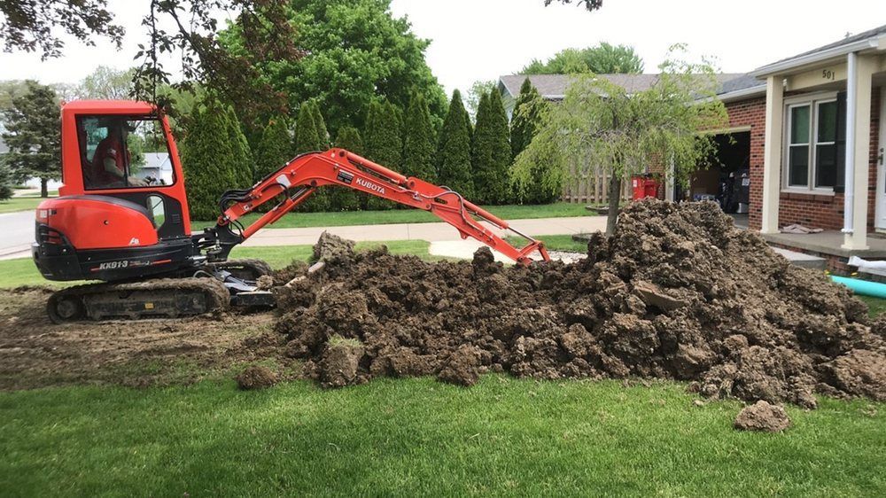 Orange excavator digging a large dirt pile beside a house on a grassy lawn
