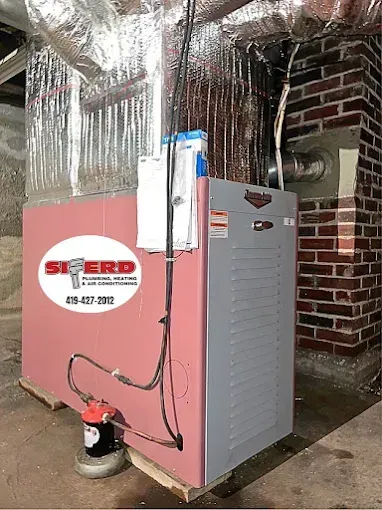 Red HVAC furnace unit in a basement with ductwork overhead and brick wall background