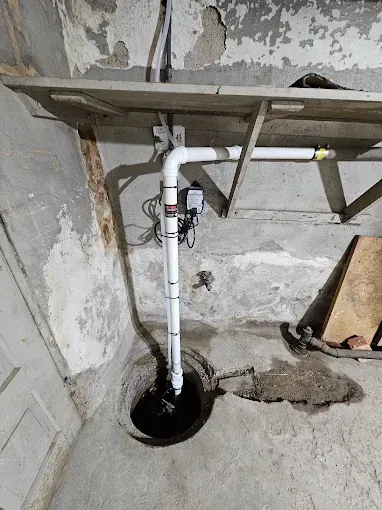 White PVC pipe draining into a floor hole in a rough concrete basement corner