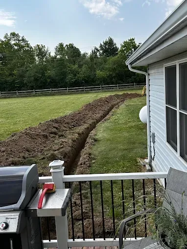 Backyard with a long trench along the lawn beside a house and porch railing