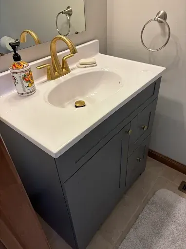 White bathroom vanity with gold faucet, soap dispenser, and mirror above a sink next to a towel ring.