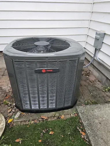 Outdoor Trane air conditioner unit beside a house wall and concrete walkway.