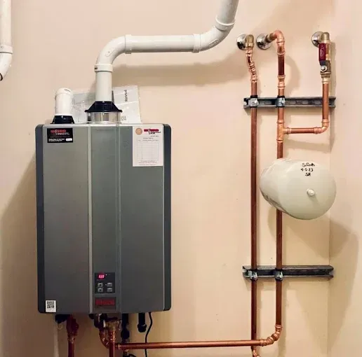 Wall-mounted tankless water heater with copper pipes and a white expansion tank in a utility room