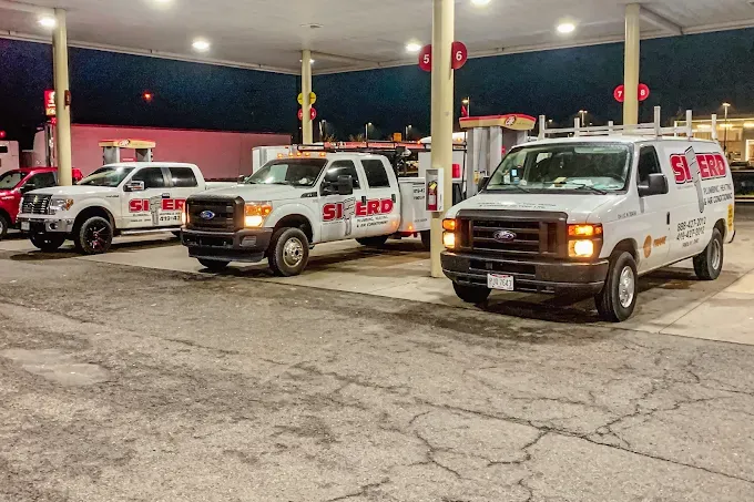 Three white service vans parked at a gas station at night under bright canopy lights.