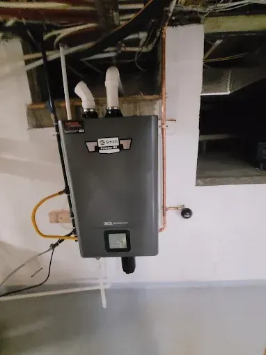 Wall-mounted gray utility box with pipes and wiring in an unfinished room.