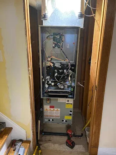 Open furnace cabinet in a hallway closet with exposed wiring and tools on the floor.