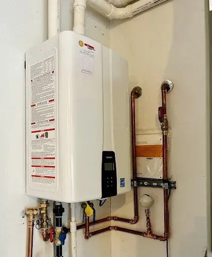 Wall-mounted white water heater with copper pipes and control panel in a utility room.