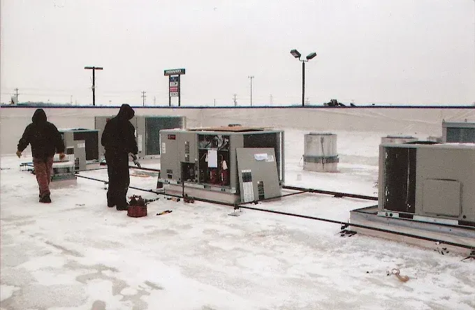 Workers inspecting rooftop HVAC units in a snowy industrial area