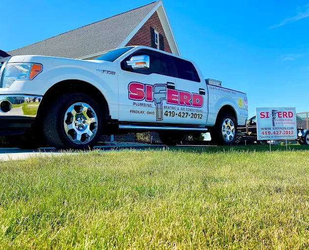 Silver pickup truck with red “SIERD” logo parked on grass beside a house under a bright blue sky