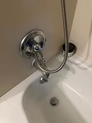Chrome handheld shower hose above white bathtub drain area