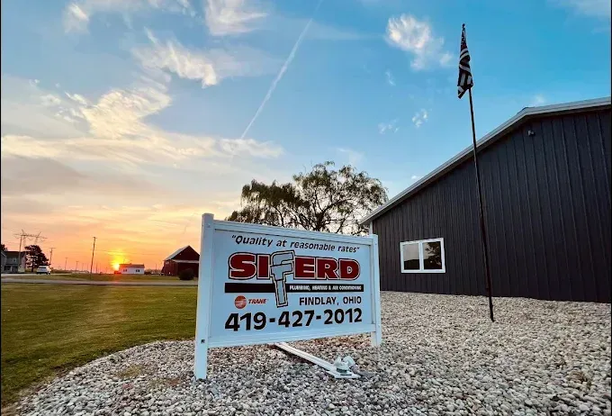 Siered sign beside a dark building at sunset, with gravel foreground and flagpole.