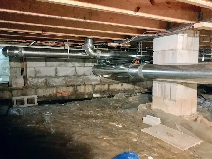 Crawlspace with exposed wooden beams, ductwork, and cinderblock foundation under a house