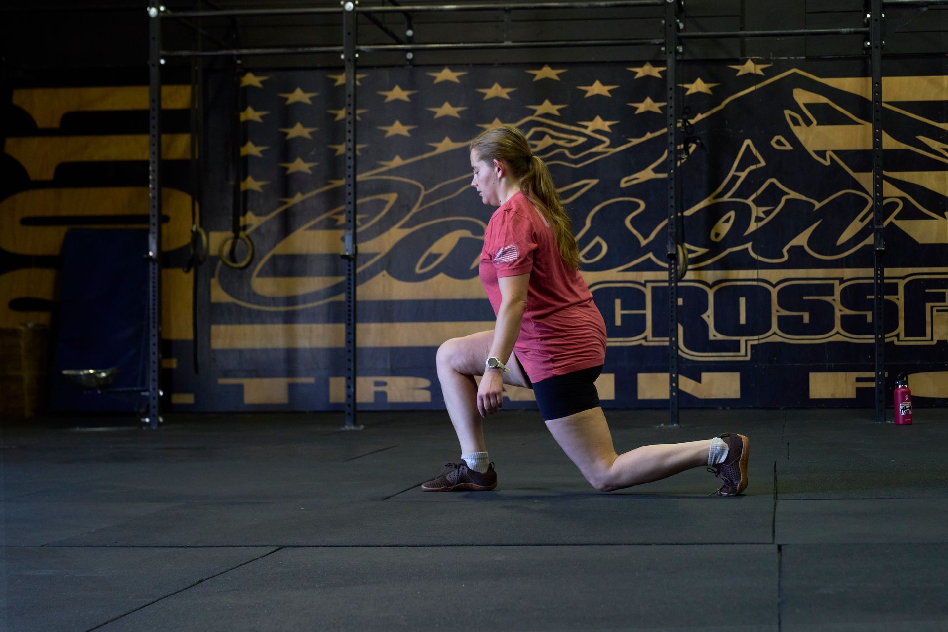Person lunging in Carson City CrossFit, a gym in Carson City, Nevada, wearing a pink shirt, in front of a CrossFit wall mural.