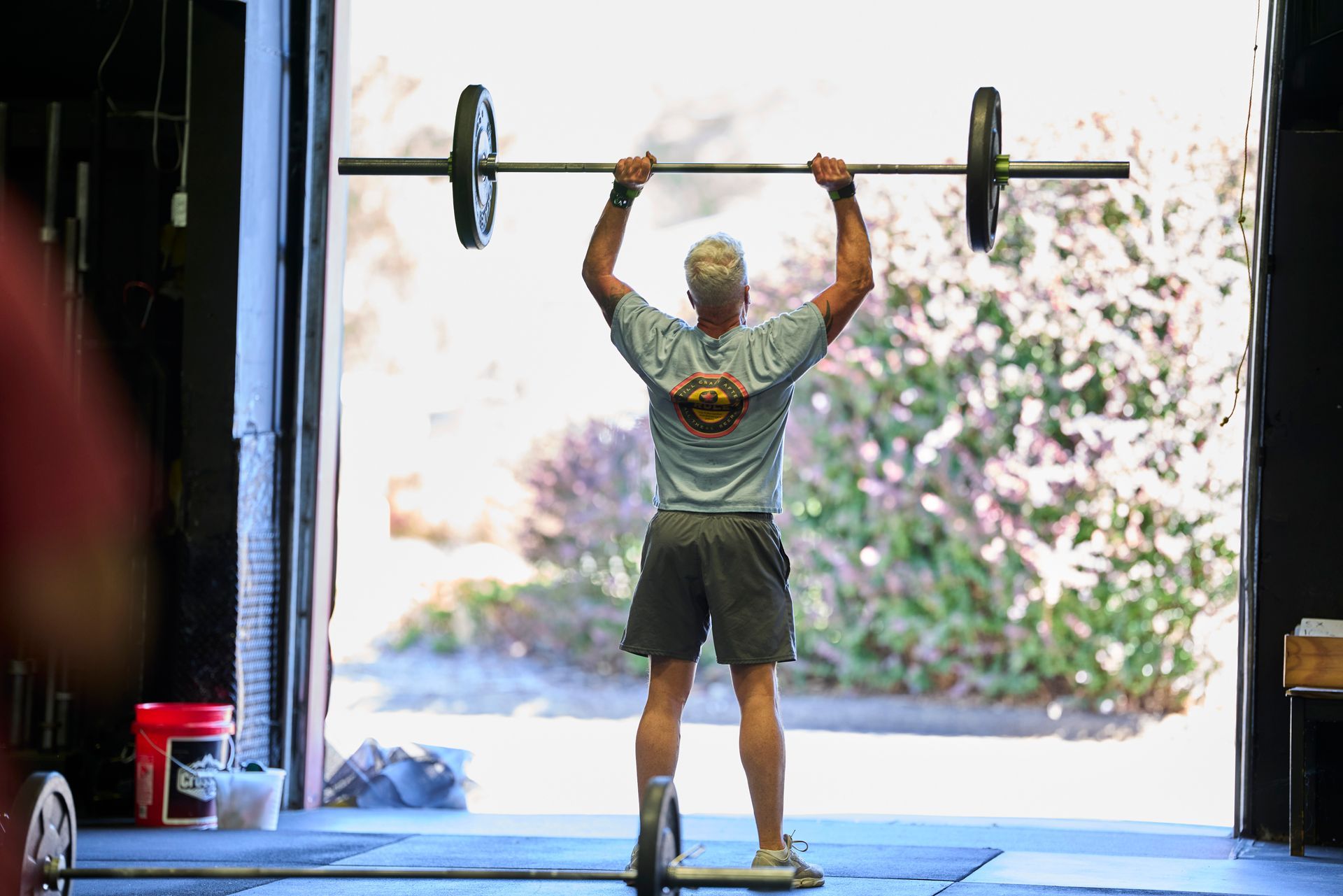 Person lifting a barbell overhead in Carson City CrossFit, a gym in Carson City, Nevada, with an open garage door and bright outdoor light.