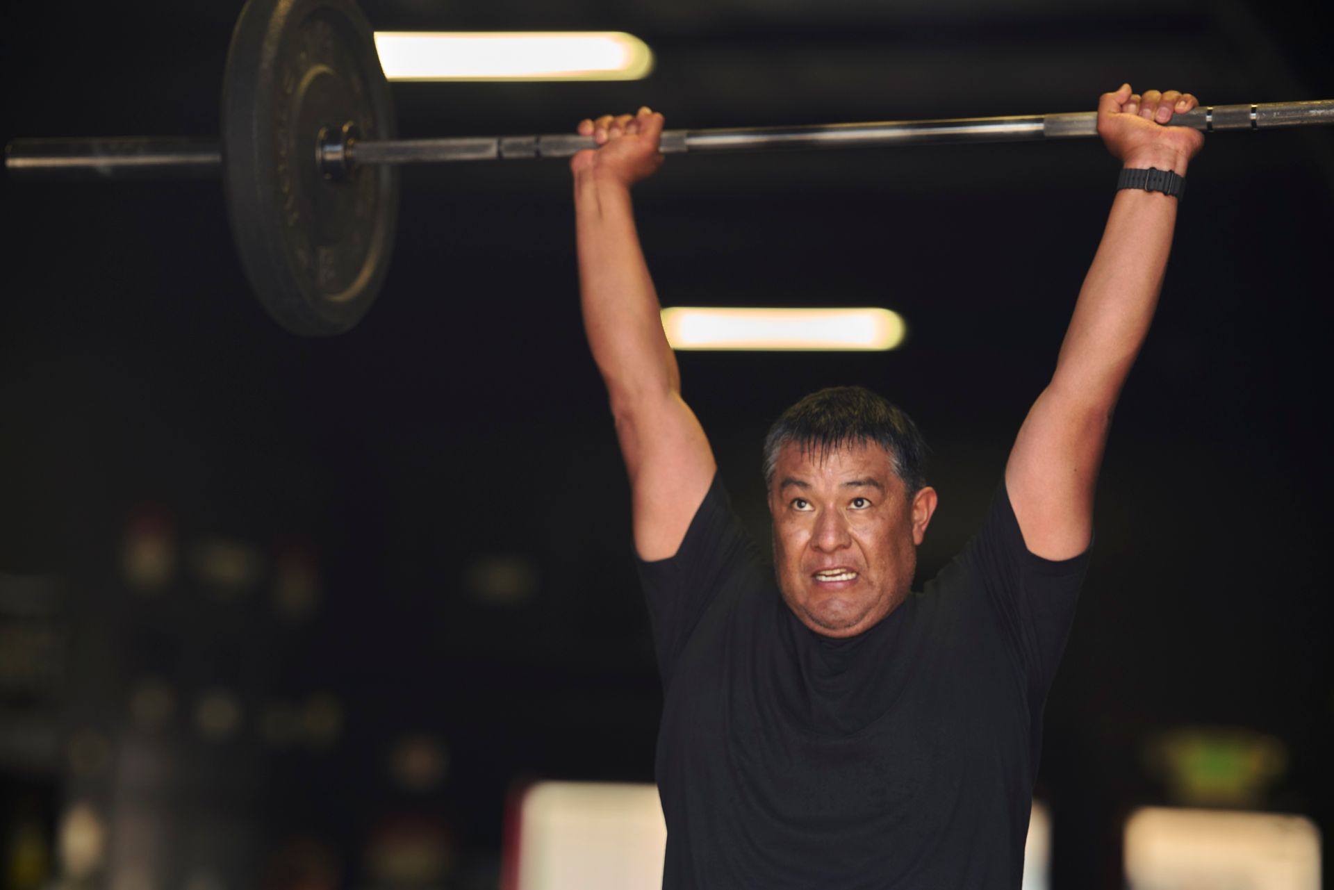 Man lifting a barbell overhead at night, straining with effort under bright lights i Carson City CrossFit, a gym in Carson City, Nevada