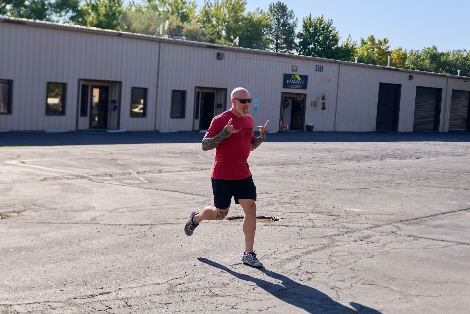 Runner in a red shirt jogging across a sunlit parking lot in front of a warehouse.