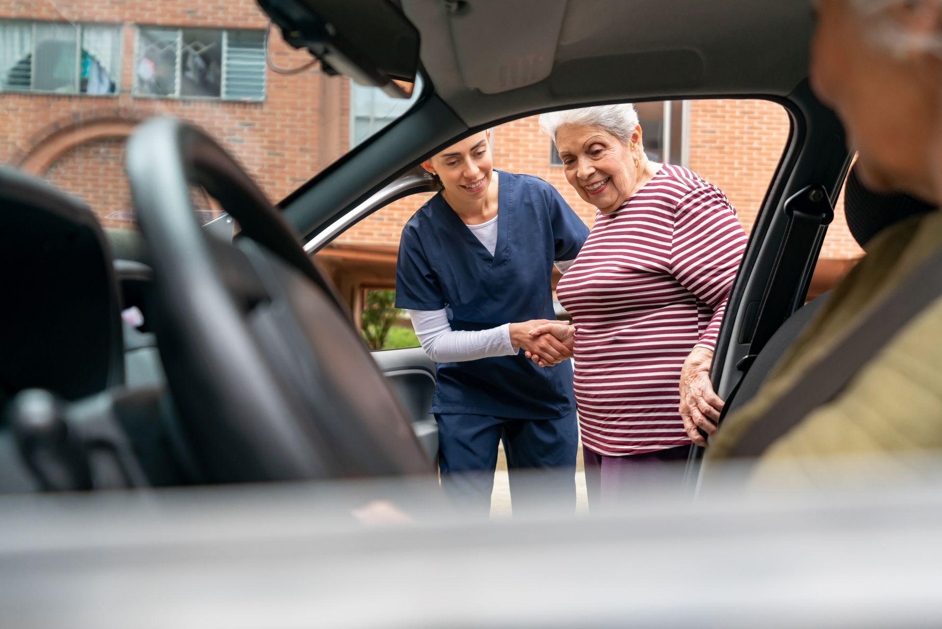 Inside a car, a woman greets an older woman with a handshake, showcasing elderly transportation
in K
