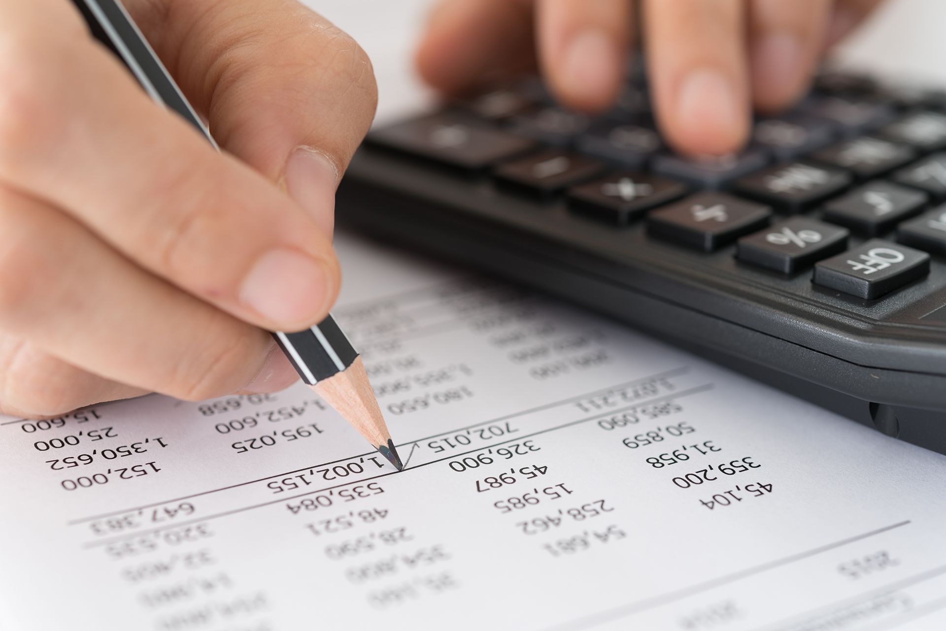 A person is writing on a piece of paper while using a calculator.