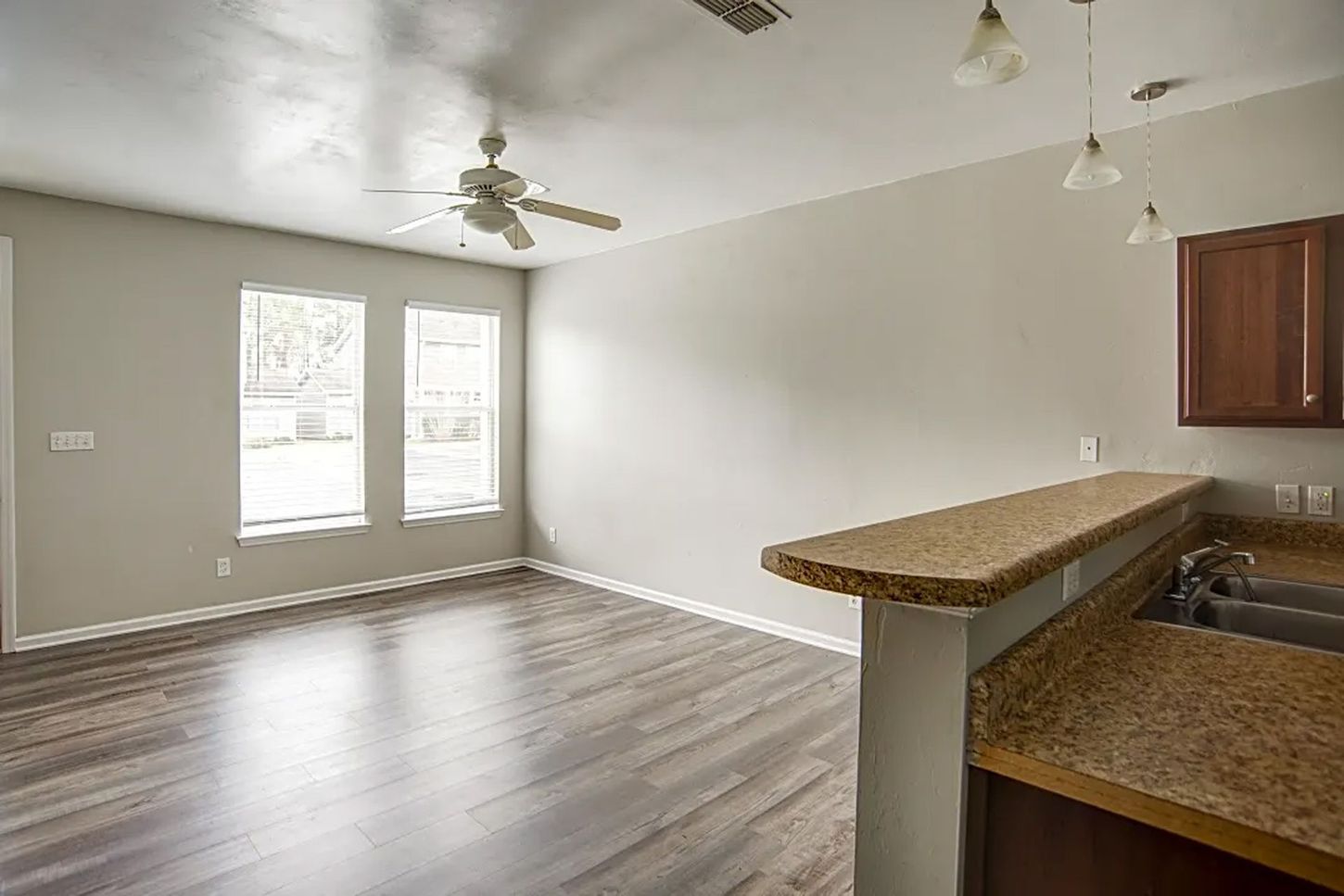 An empty living room with hardwood floors and a ceiling fan.
