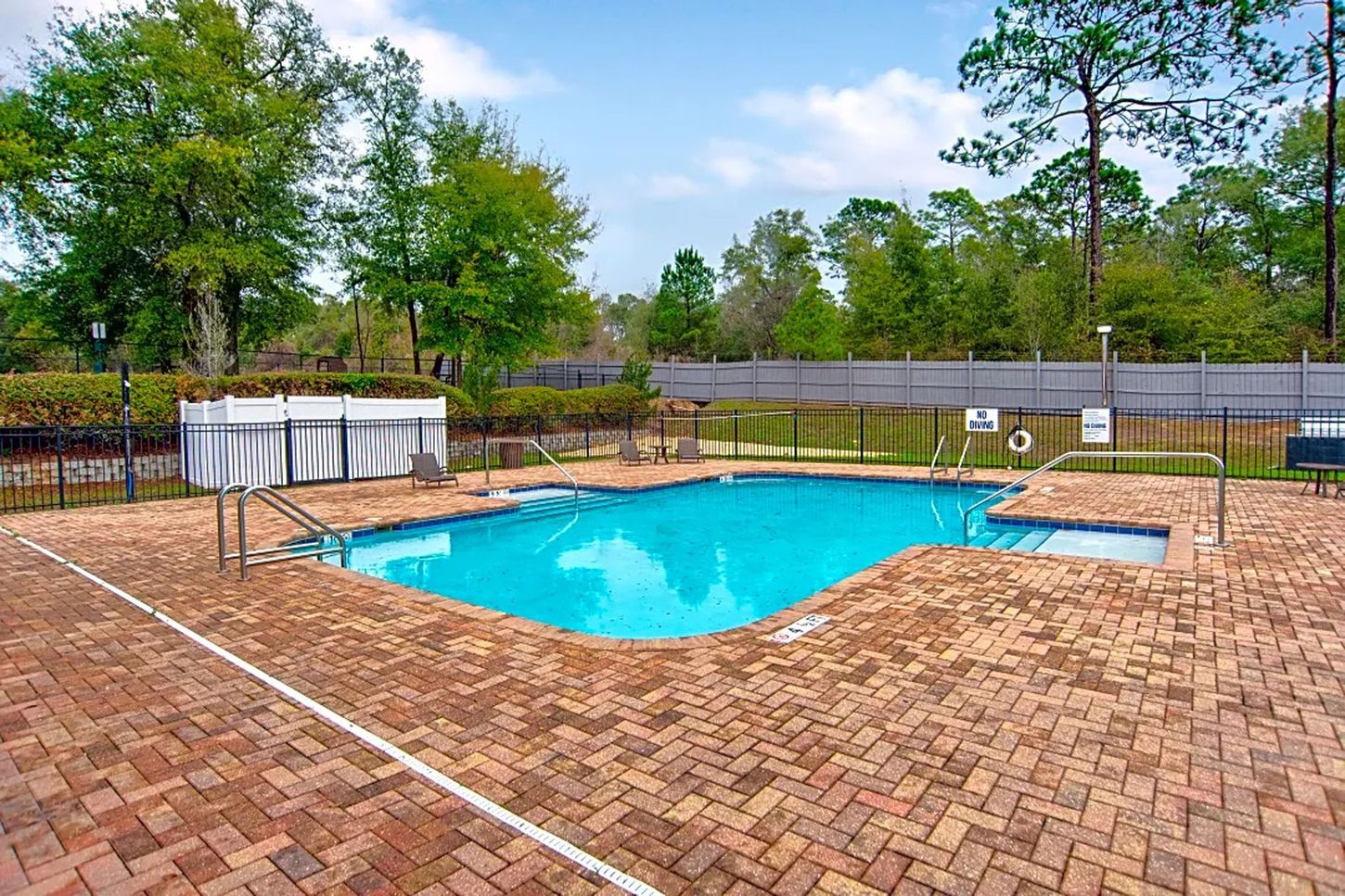 A large swimming pool is surrounded by bricks and trees.
