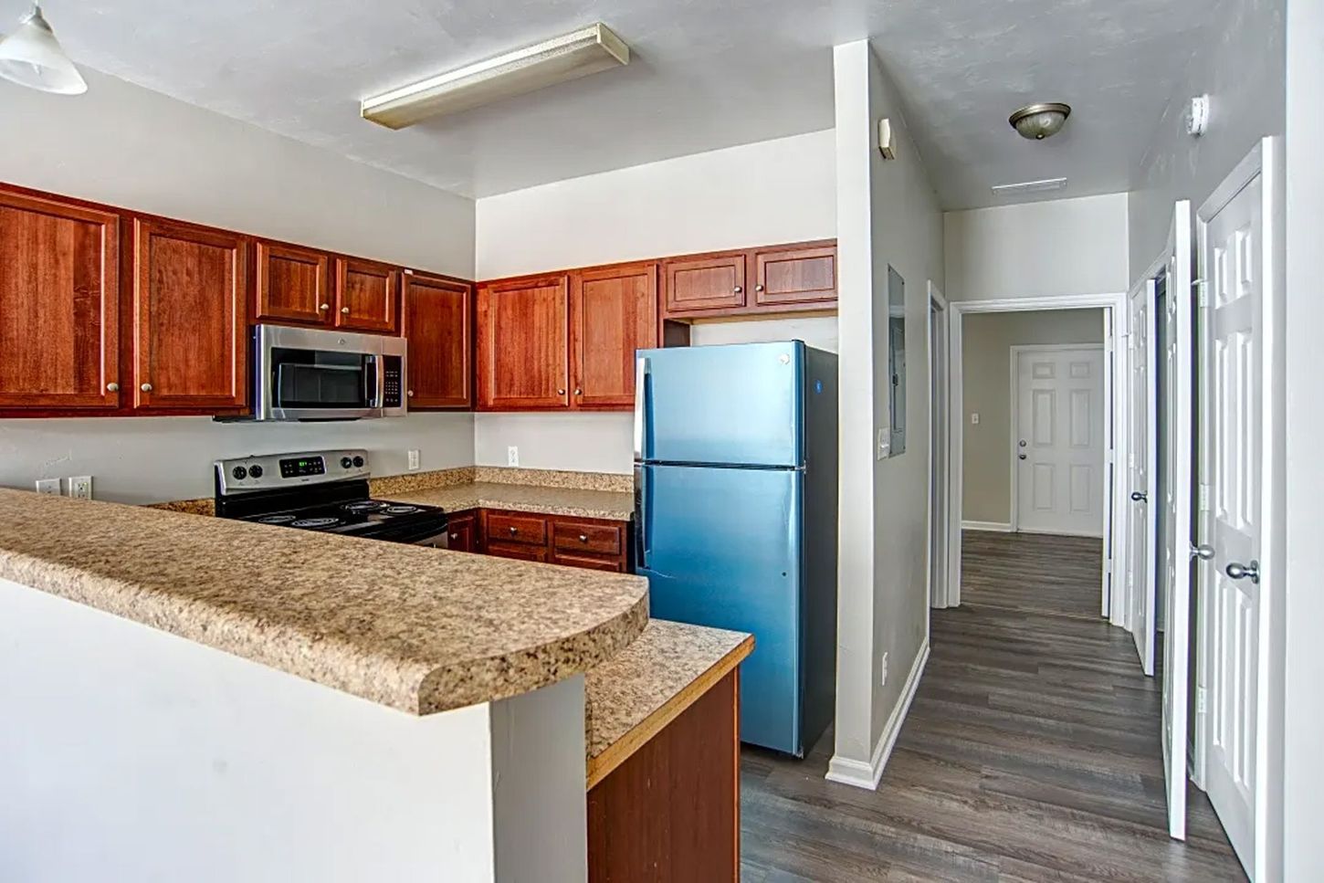 A kitchen with a blue refrigerator , stove and microwave.