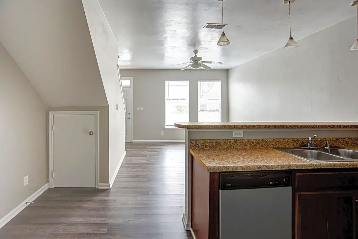 An empty kitchen with a sink , dishwasher , and ceiling fan.