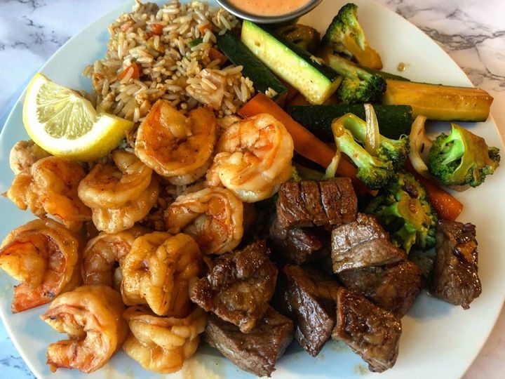 A plate of food with shrimp , steak , rice and vegetables on a table. A plate of food with shrimp , steak , rice and vegetables on a table.