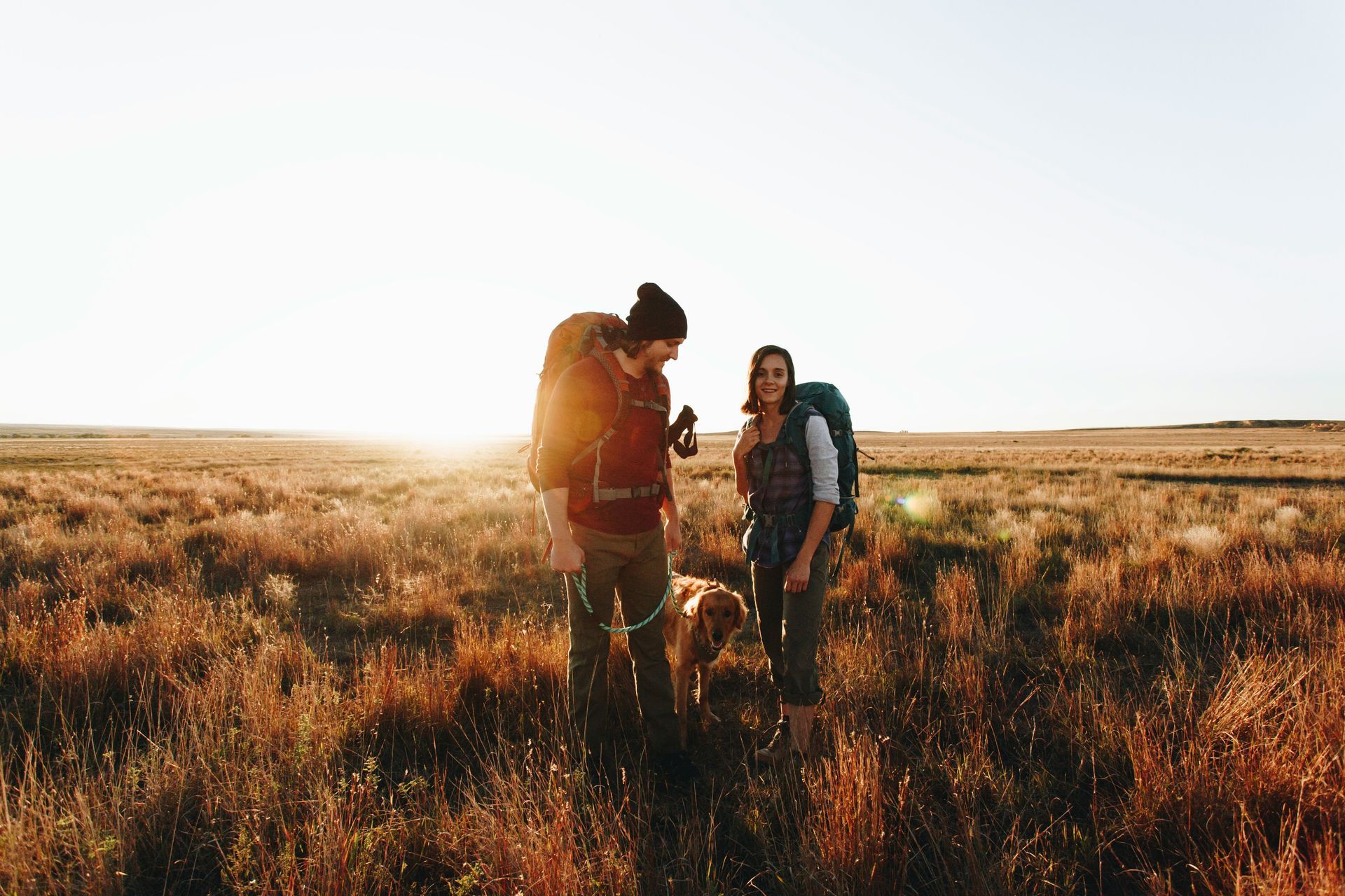 Two hikers with backpacks standing in a sunlit field at sunset