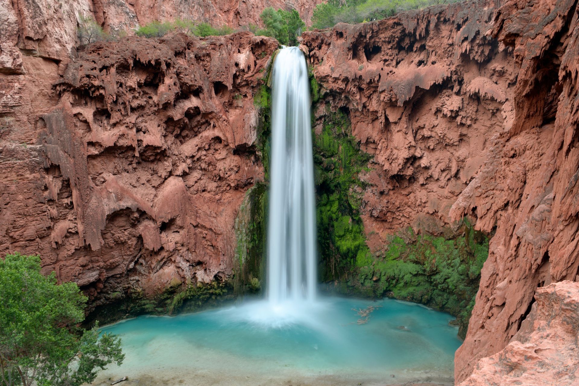 Waterfall plunging into a turquoise pool between red canyon walls