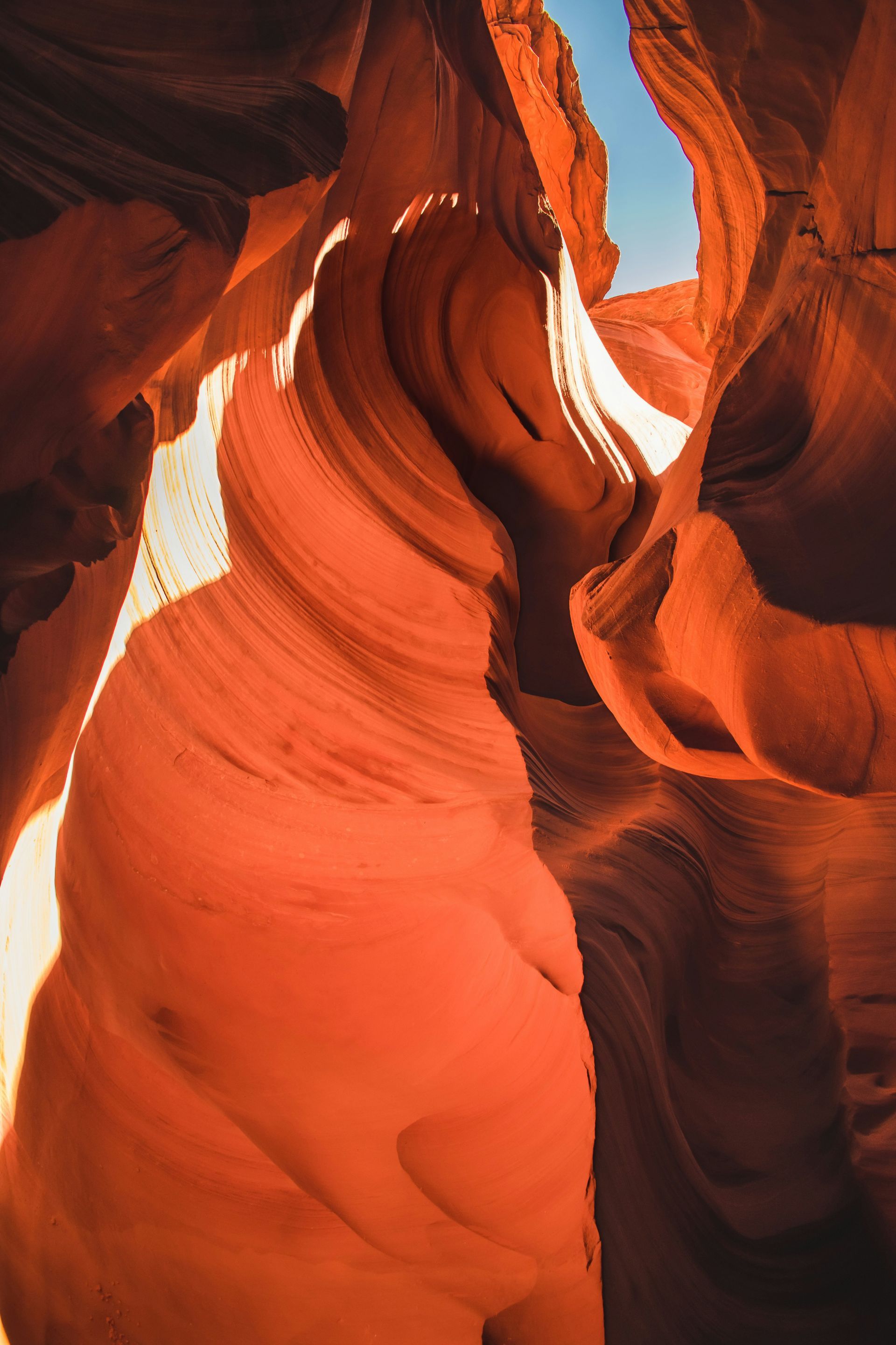 Red sandstone canyon with sculpted, wavy rock walls and sunlight streaming through a narrow opening.