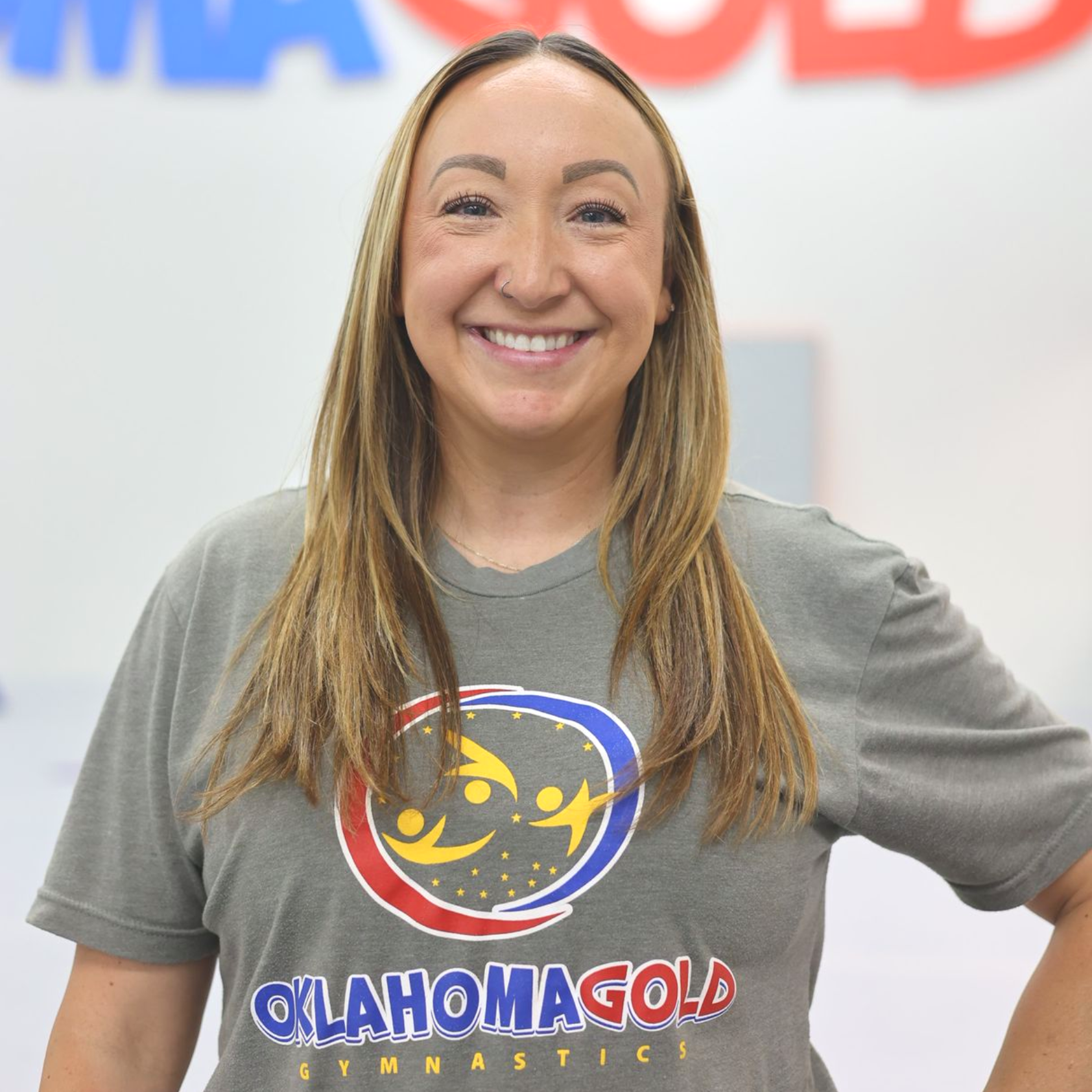Smiling woman in a gray Oklahoma Gold T-shirt standing against a white background