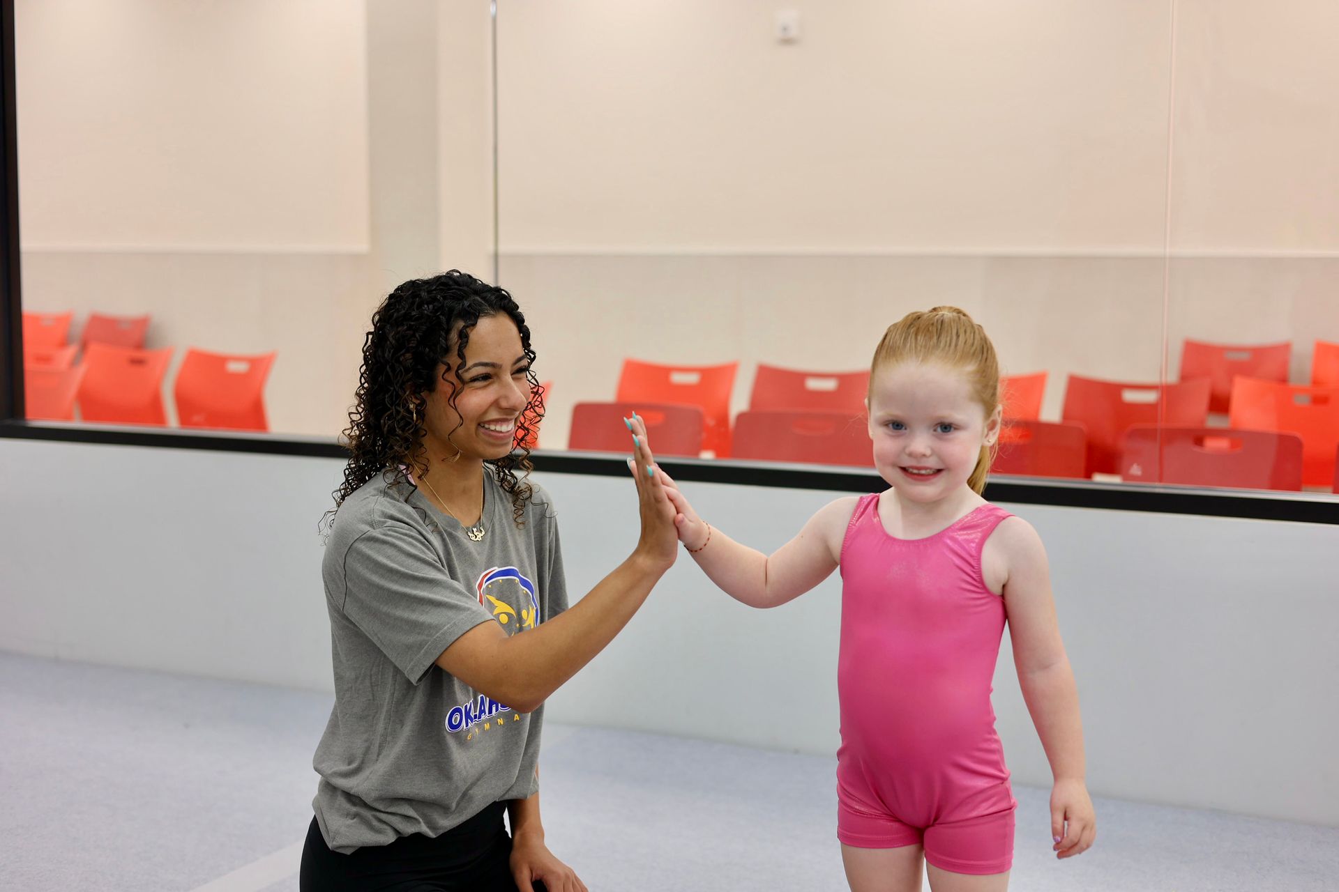 Woman and child high-five in a dance studio with red chairs in the background