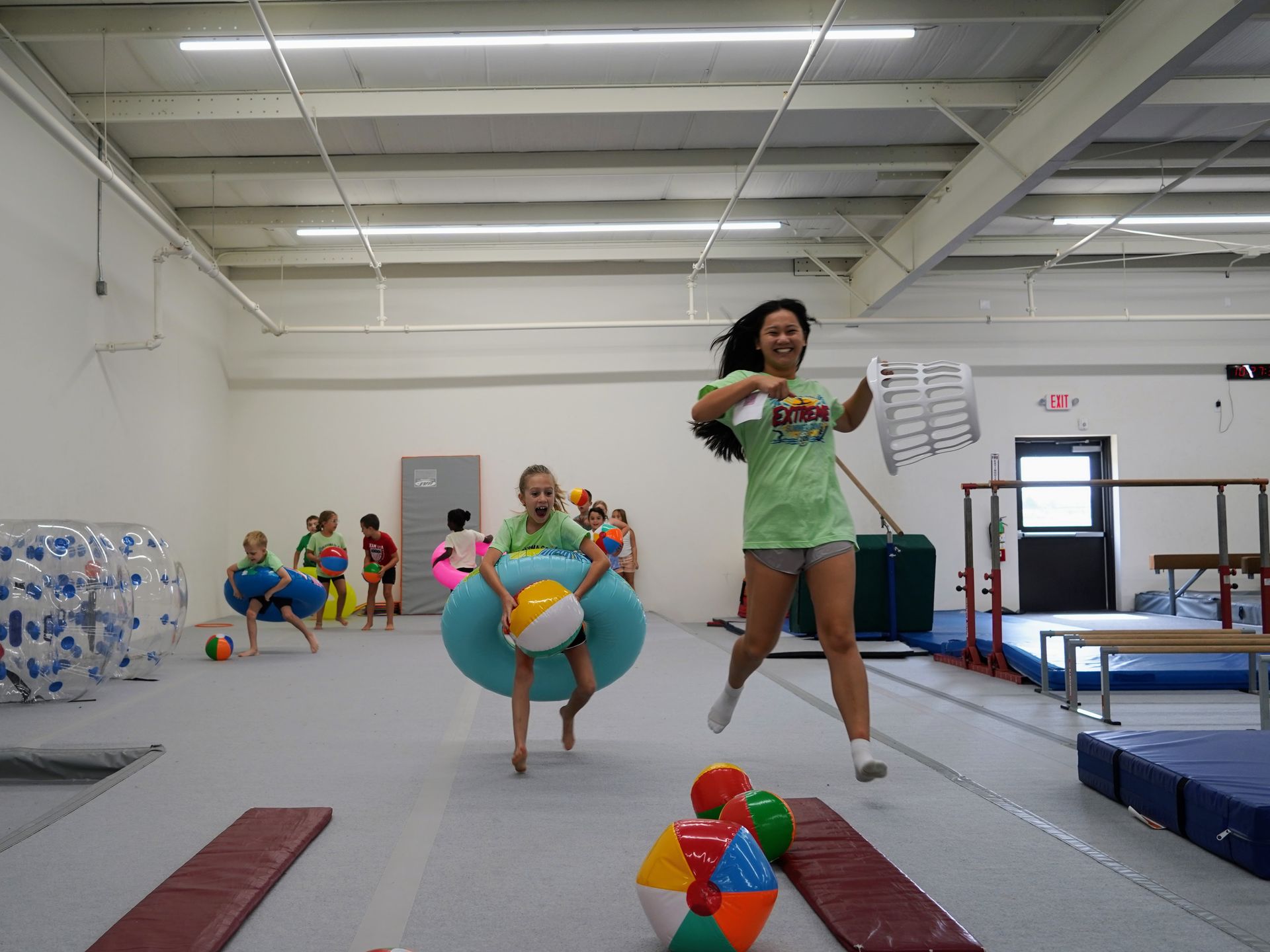Children playing in a gym, running with colorful balls and cones under bright overhead lights