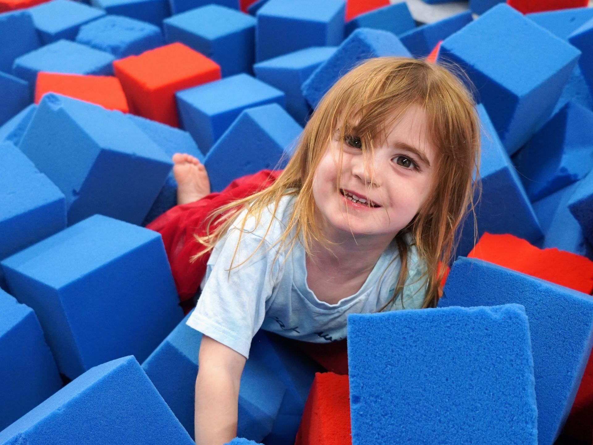 Smiling child in a blue foam pit with red and blue blocks