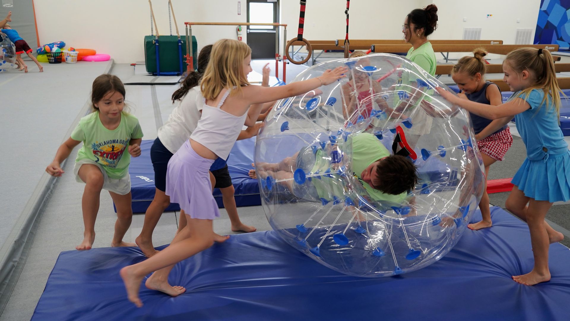 Children playing inside and pushing a clear inflatable ball on a blue gym mat