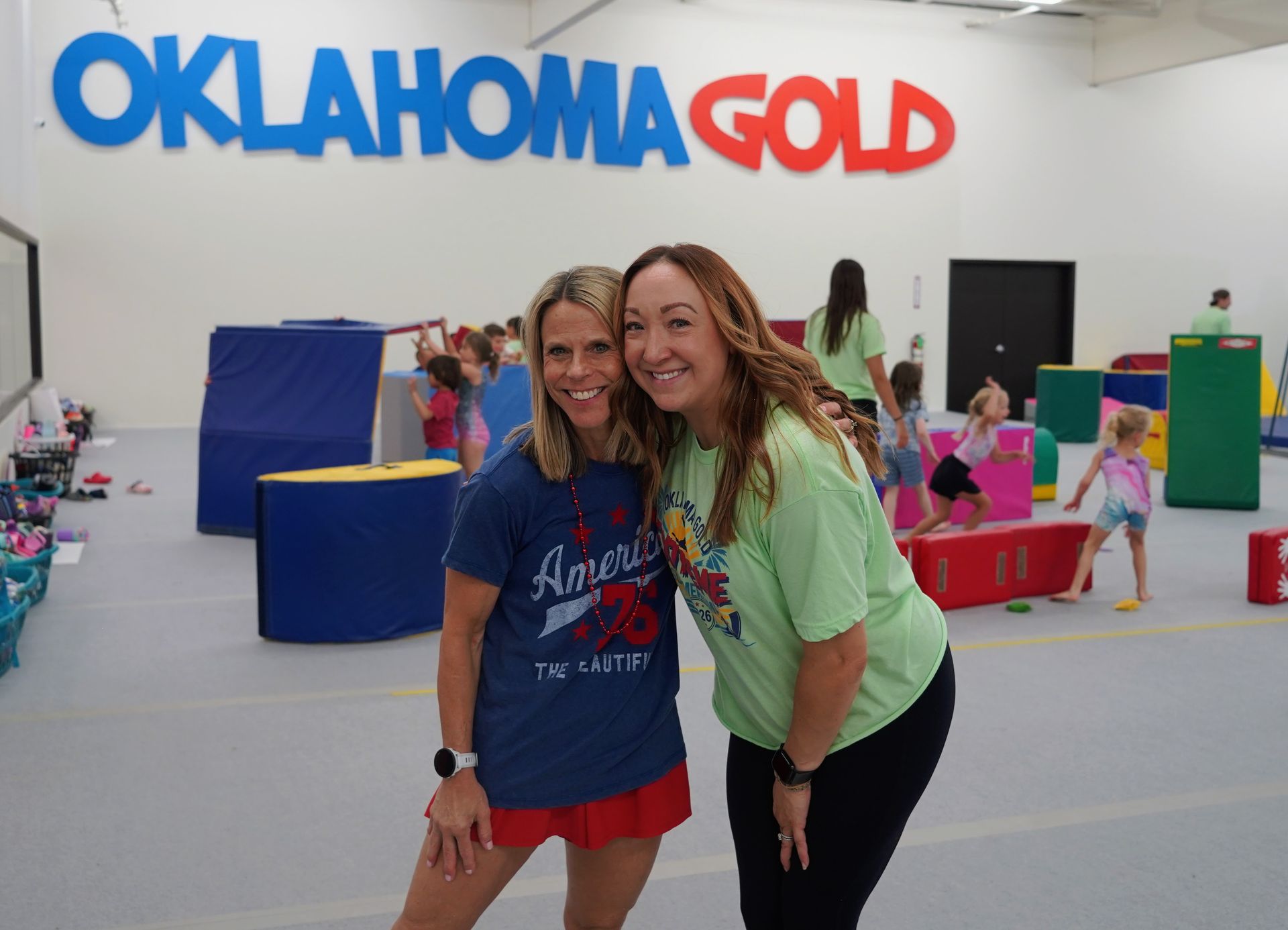 Two women smiling at an Oklahoma Gold event with colorful play structures in the background