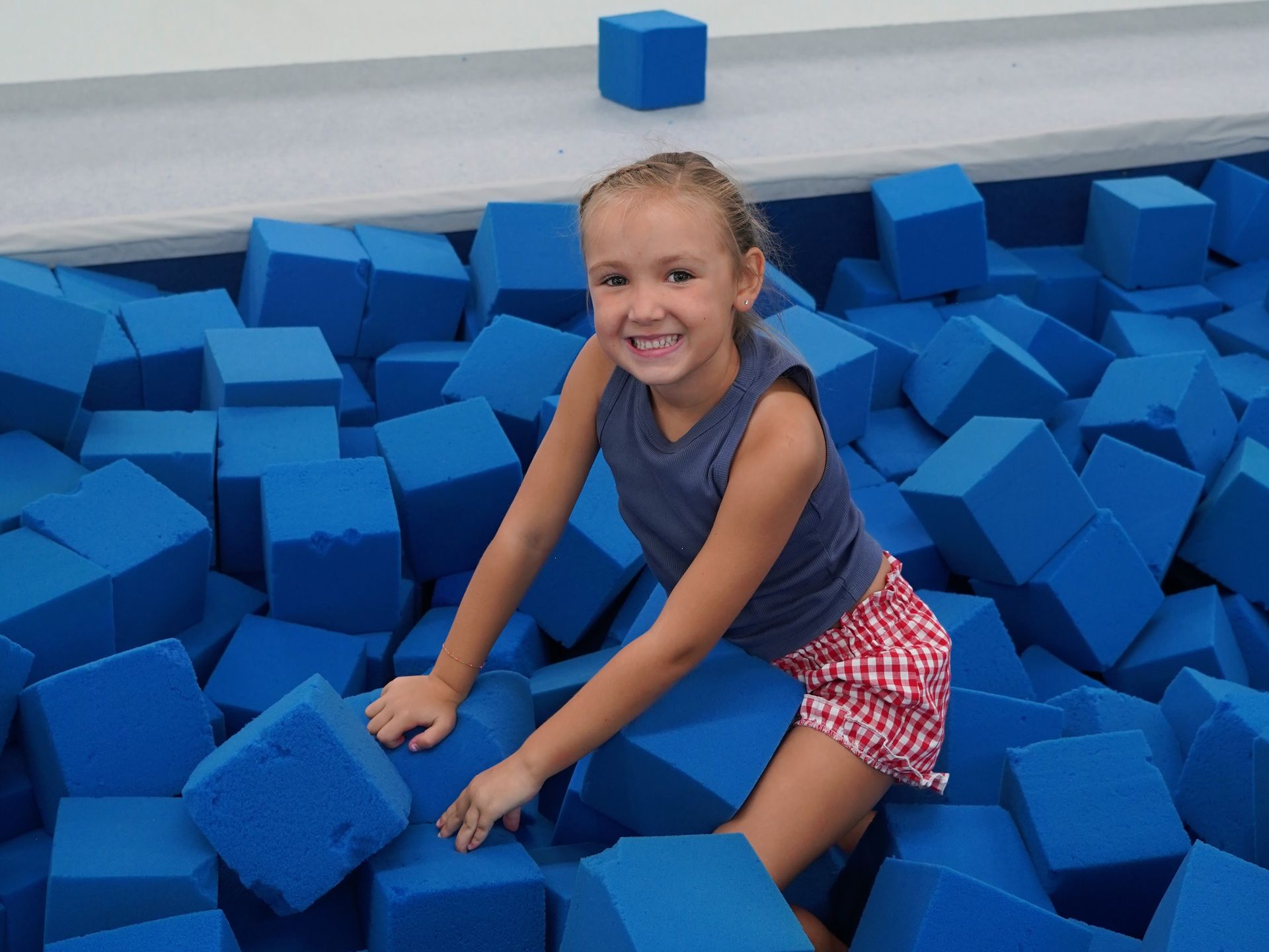 Smiling girl sitting in a foam pit surrounded by blue foam blocks
