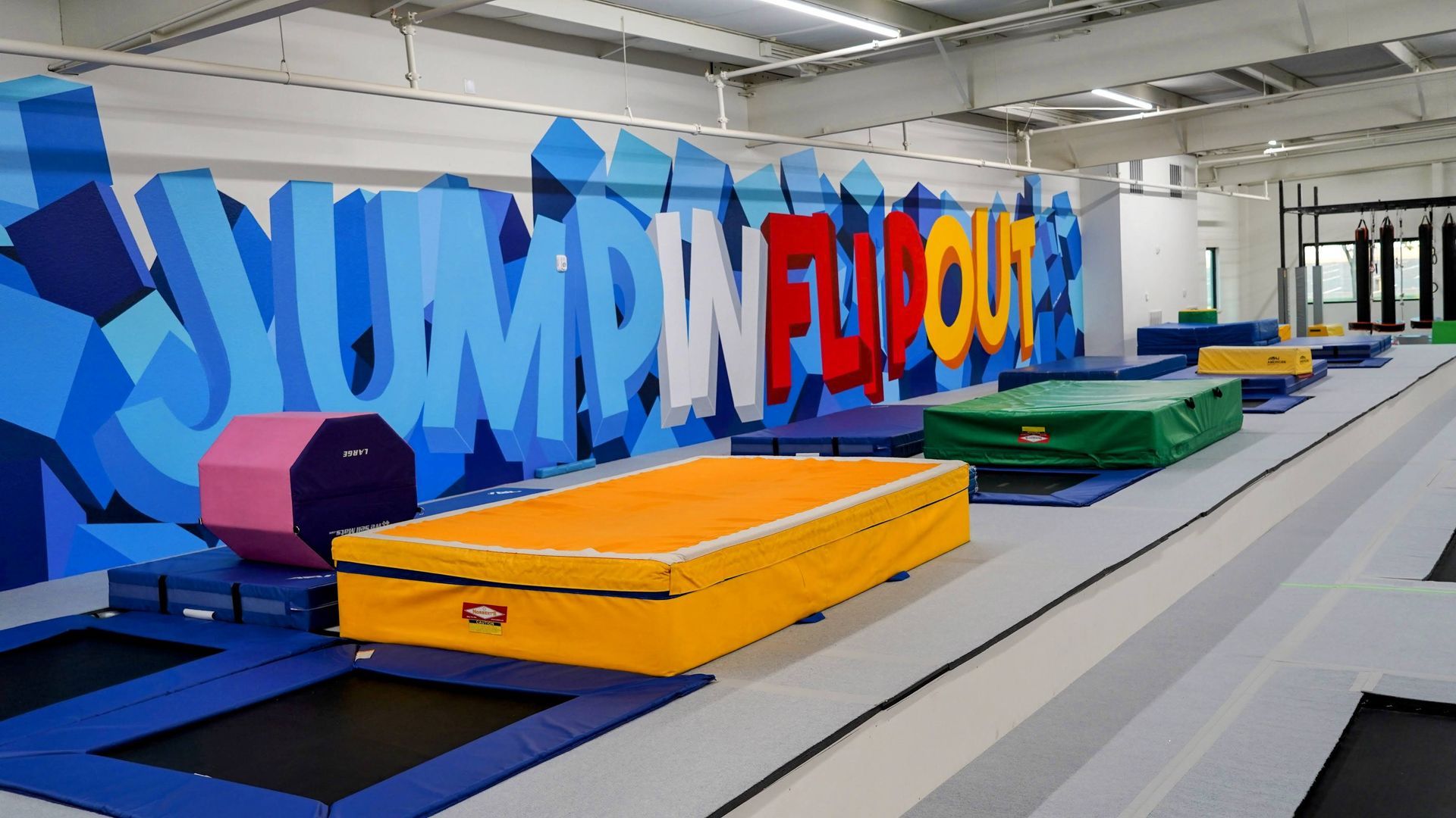 Indoor trampoline park with colorful foam pits and giant “JUMP IN FLIP OUT” letters on the wall