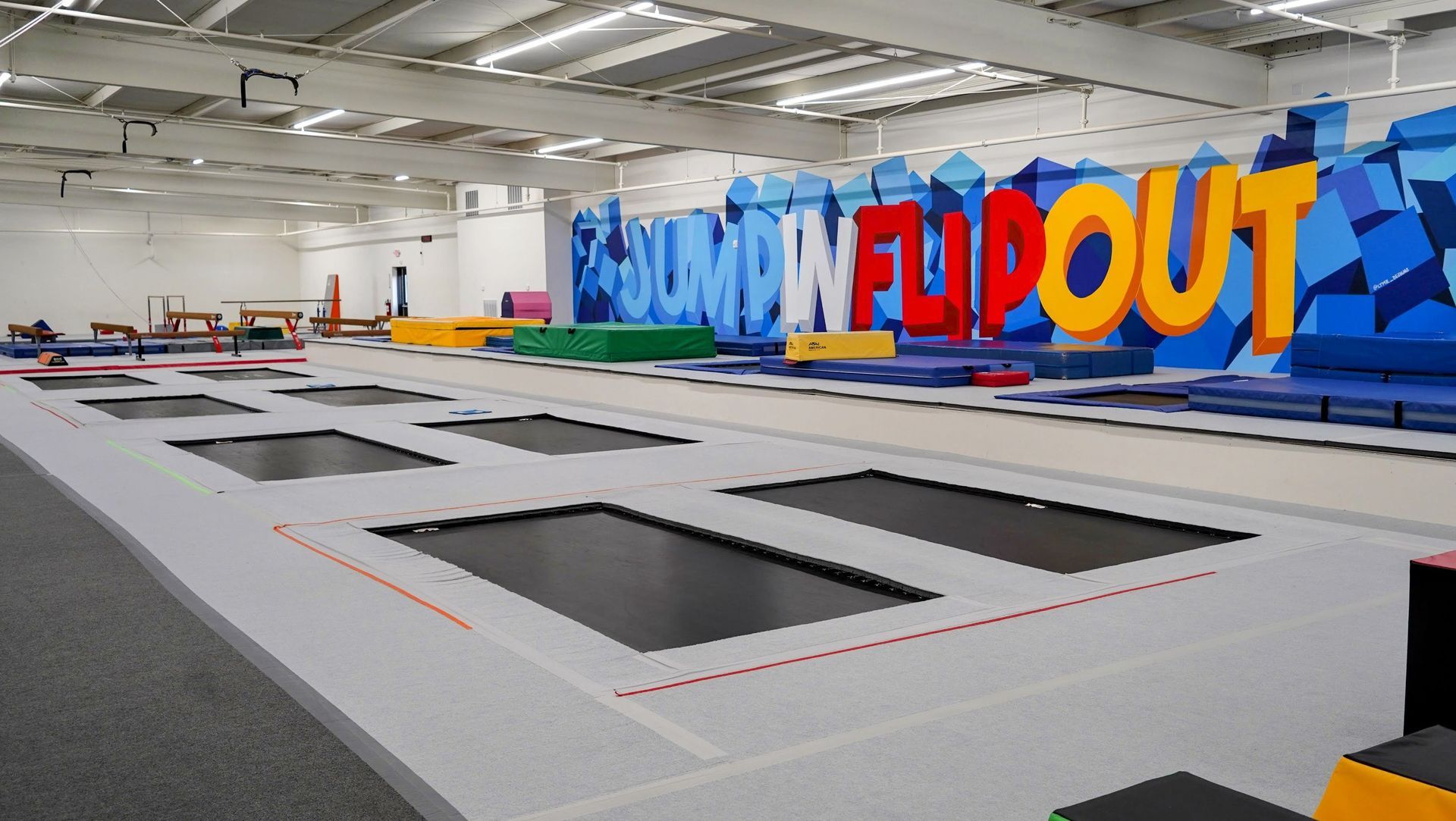 Indoor trampoline park with rows of black trampolines and colorful 