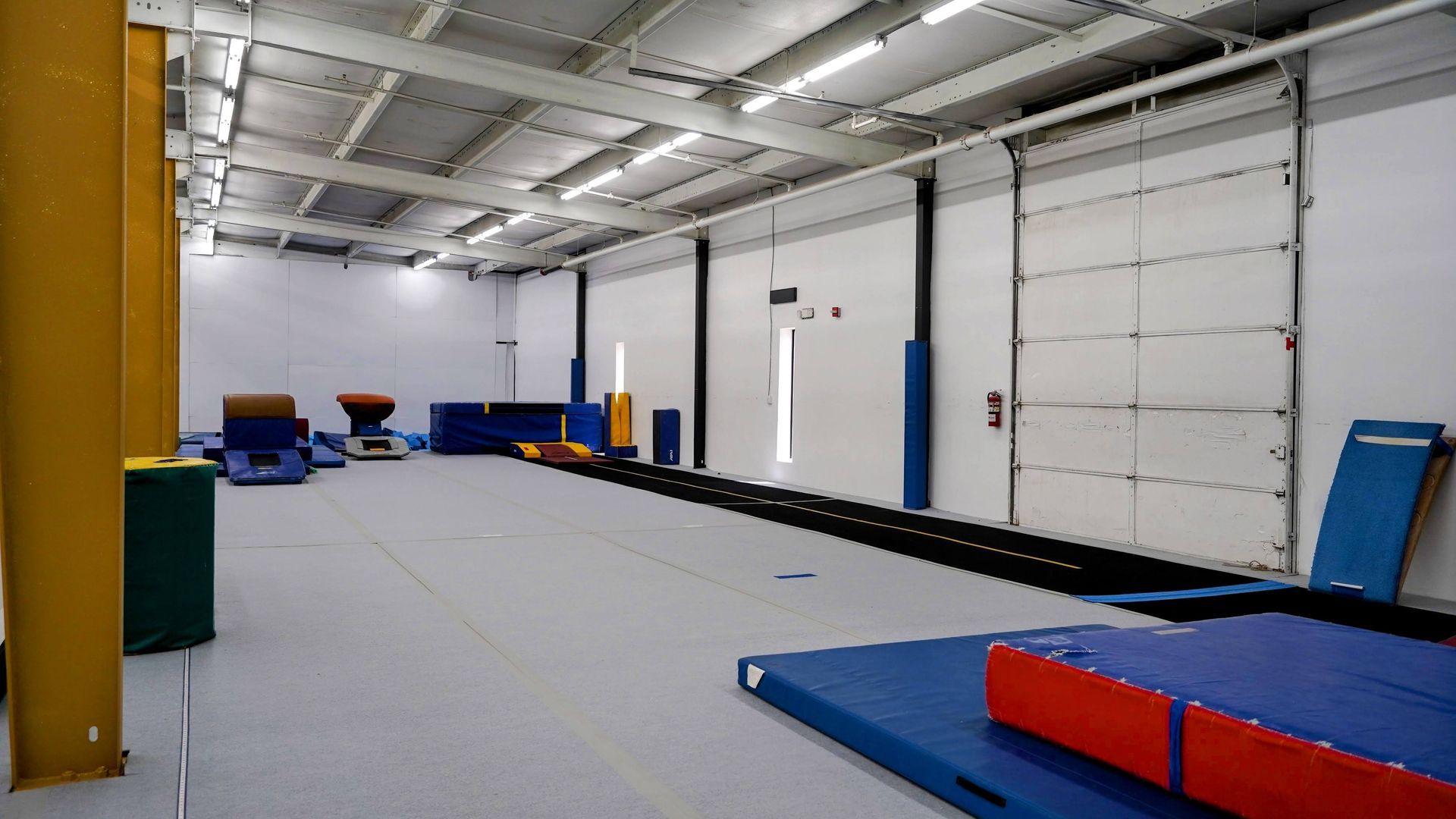 Empty indoor gymnastics gym with mats, foam blocks, and large garage-style doors