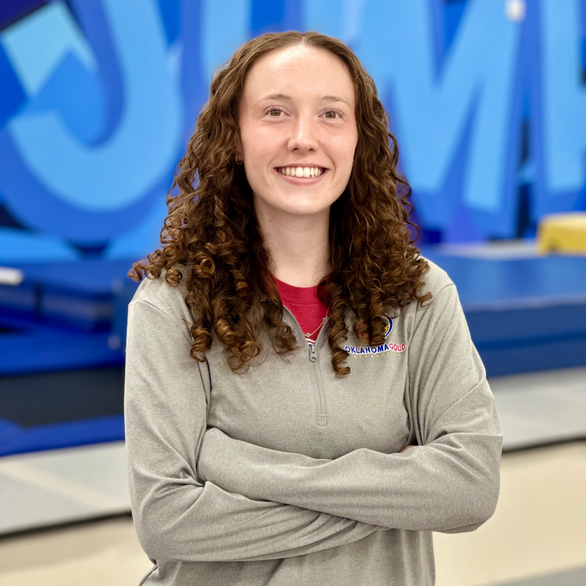 Smiling person with crossed arms in a gray sweatshirt, standing before a blue studio backdrop.